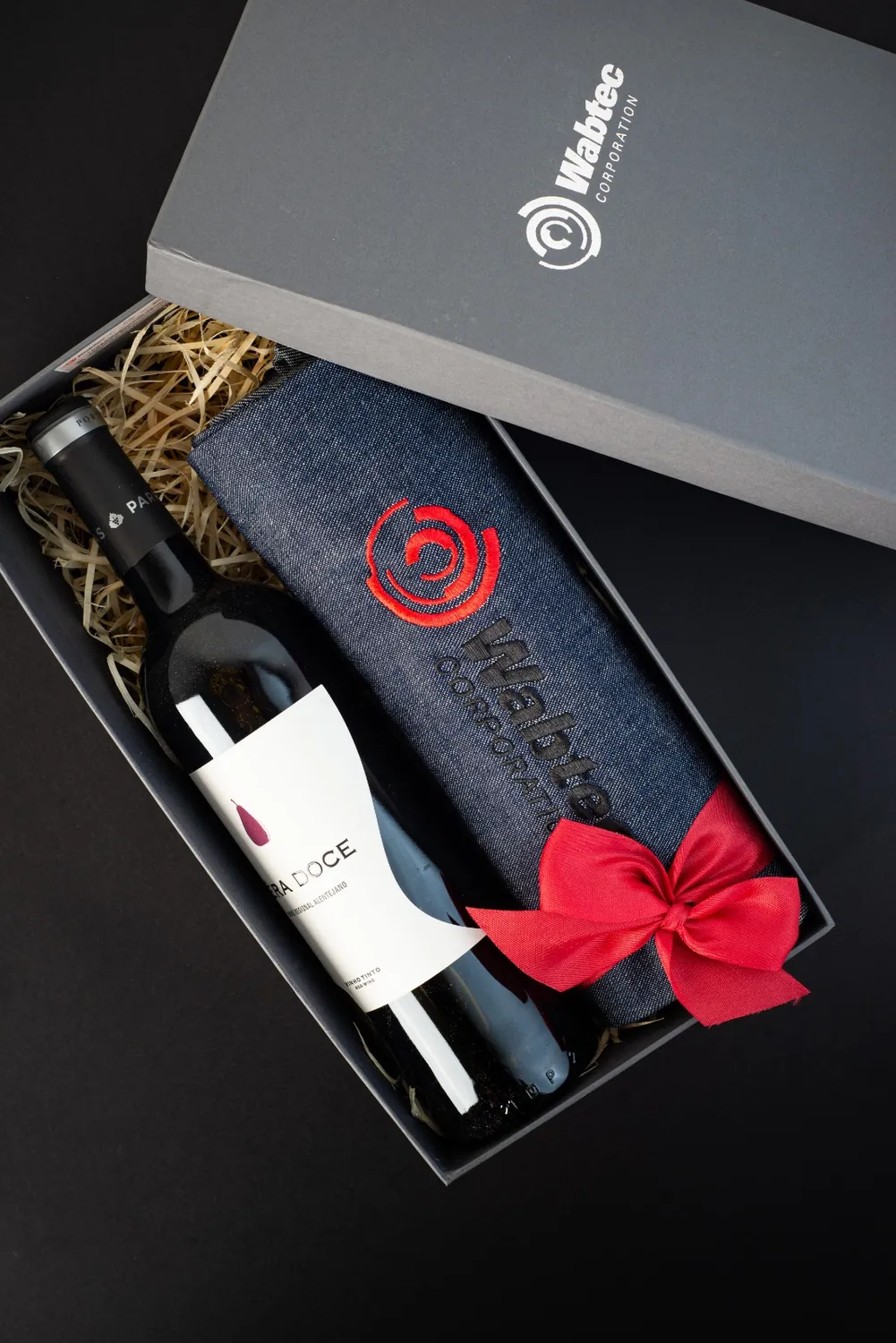 Kit com vinho, avental bordado e laço vermelho em caixa cinza